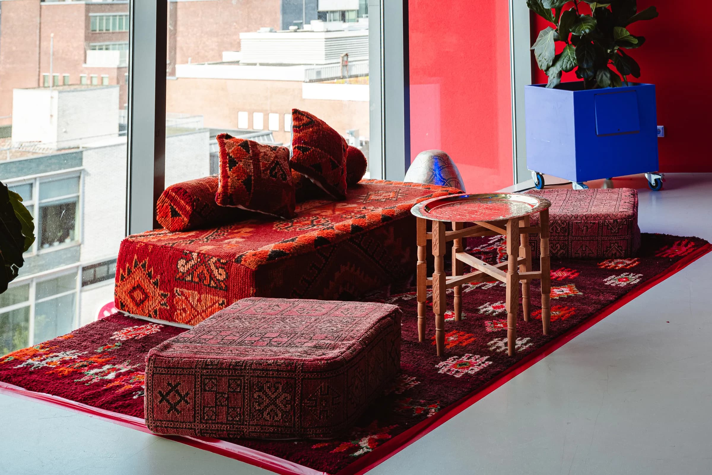 Rode gedrapeerde daybed met kilimkussens, houten bijzettafel en poef voor een raam